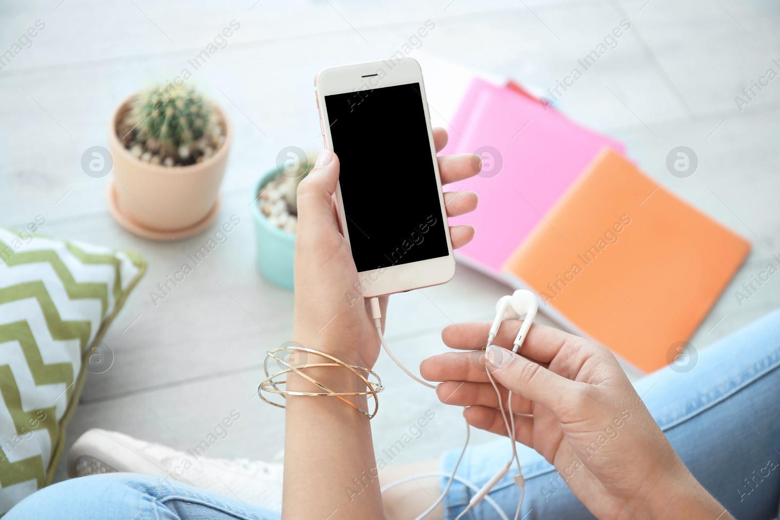 Photo of Young woman holding mobile phone with blank screen and earphones in hands, indoors