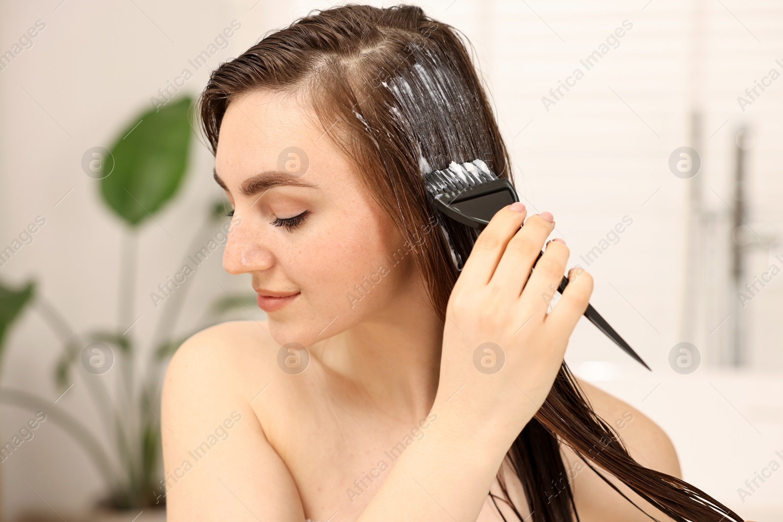 Photo of Young woman applying hair mask in bathroom