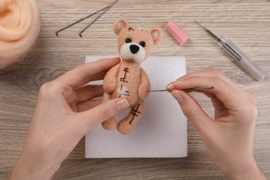 Photo of Woman felting cute toy bear from wool at wooden table, top view