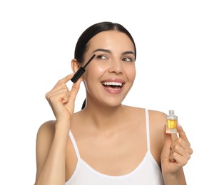 Photo of Young woman applying oil onto eyelashes on white background
