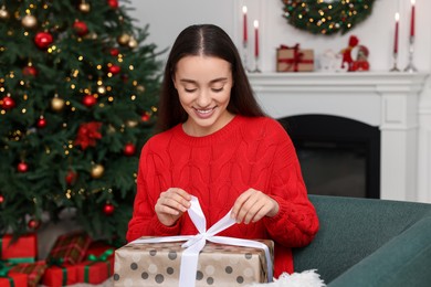 Photo of Happy young woman opening Christmas gift at home