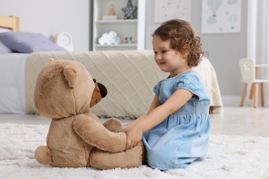 Photo of Cute little girl with teddy bear on floor at home