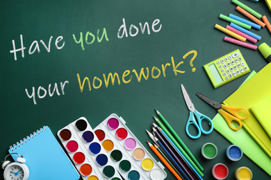 Image of School stationery and phrase HAVE YOU DONE YOUR HOMEWORK? on chalkboard, flat lay 