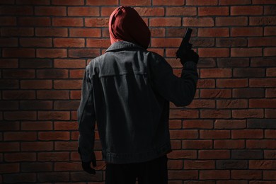 Thief in hoodie with gun against red brick wall, back view