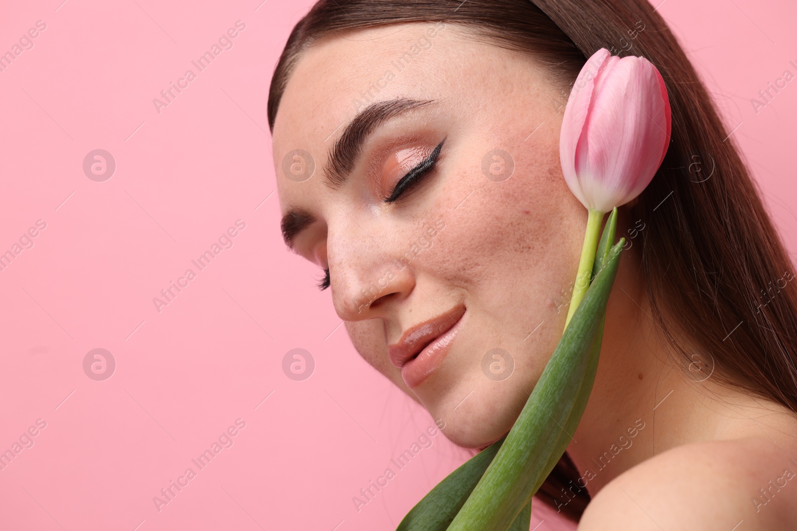 Photo of Beautiful woman with fake freckles and tulip on pink background, closeup. Space for text