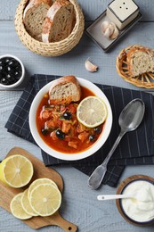 Photo of Meat solyanka soup with sausages, olives and vegetables served on grey wooden table, flat lay