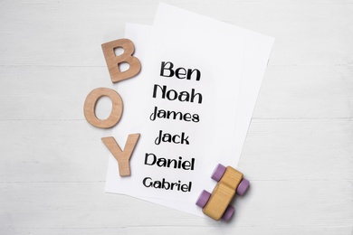 List of baby names, toy and wooden letters on white table, flat lay