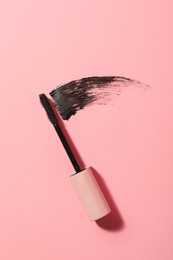 Photo of Mascara wand and smear on pink background, top view. Makeup product