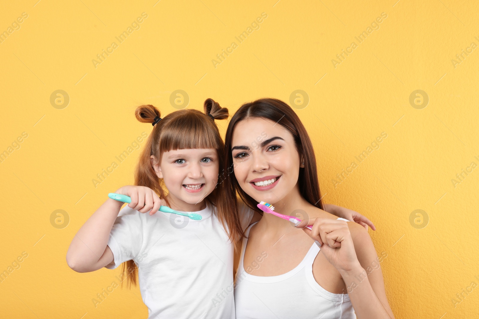 Photo of Little girl and her mother brushing teeth together on color background