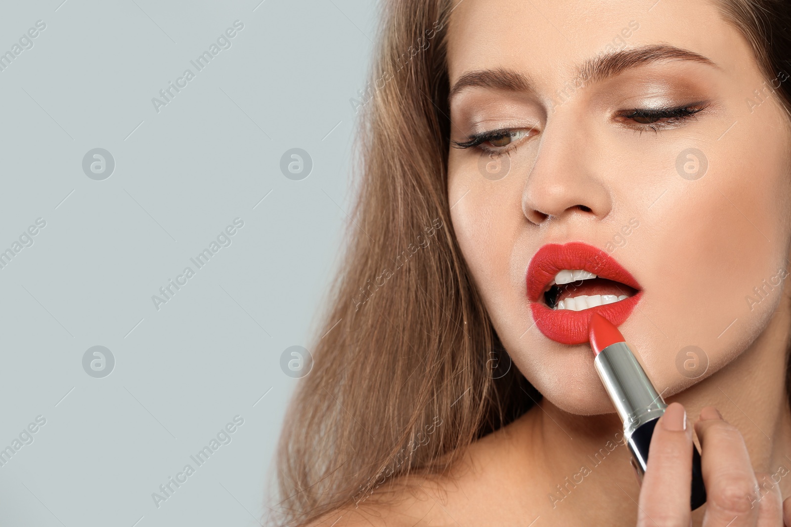 Photo of Young woman applying red lipstick on gray background. Space for text