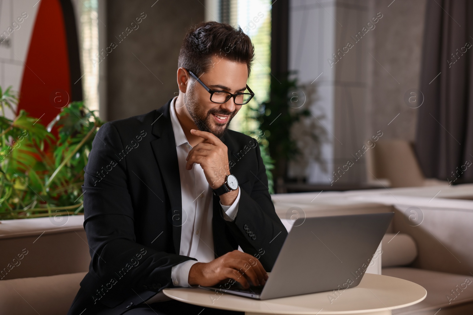 Photo of Happy young man with glasses working on laptop at table in office