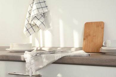 Cotton towels, board and dishware on wooden table in kitchen