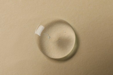Photo of Drop of cosmetic oil on beige background, top view