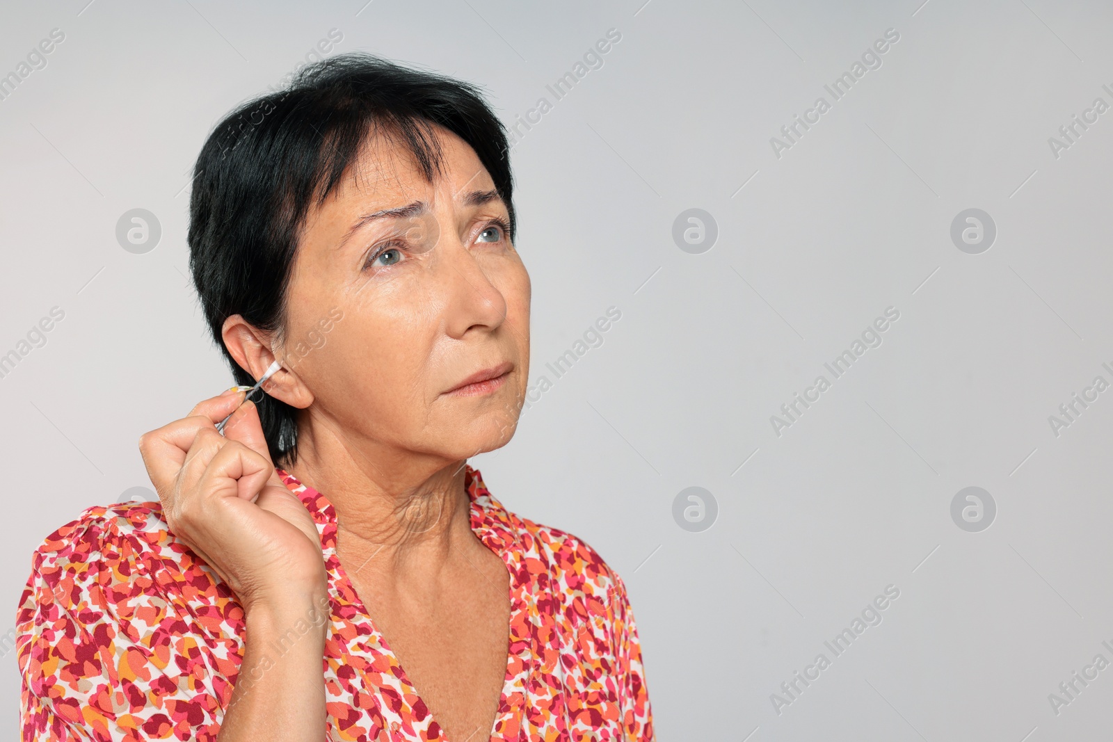 Photo of Senior woman cleaning ear with cotton swab on light grey background. Space for text