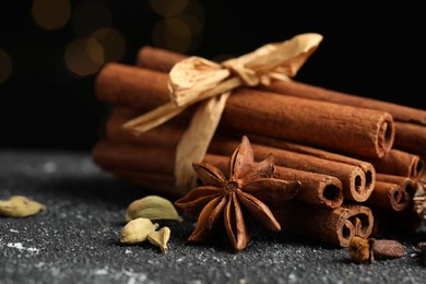 Photo of Different aromatic spices on grey textured table against black background, closeup