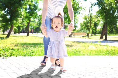 Photo of Adorable baby girl holding mother's hands while learning to walk outdoors