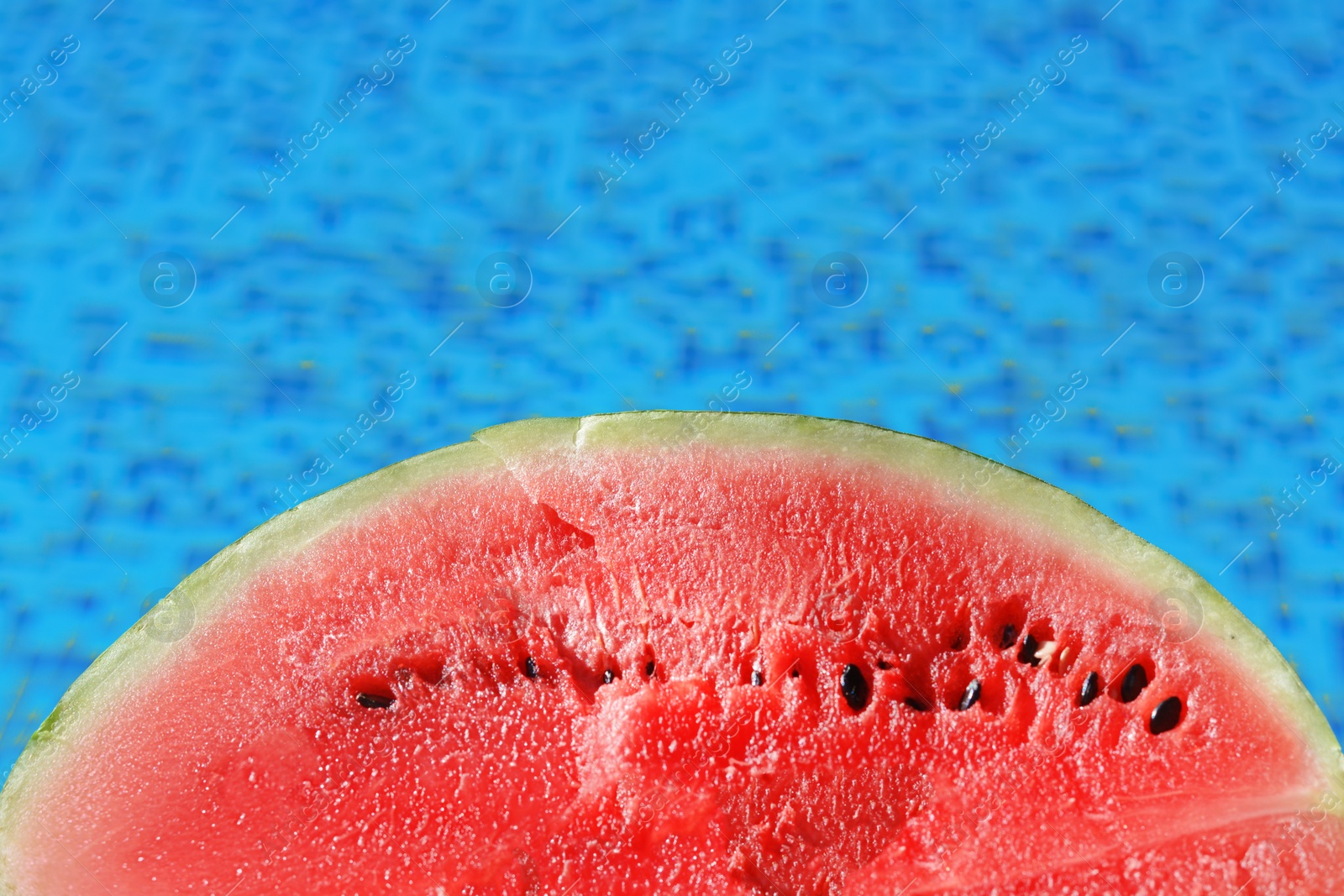 Photo of Half of fresh juicy watermelon near swimming pool outdoors, closeup. Space for text