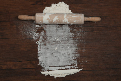 Photo of Flour and rolling pin on wooden table, top view. Space for text