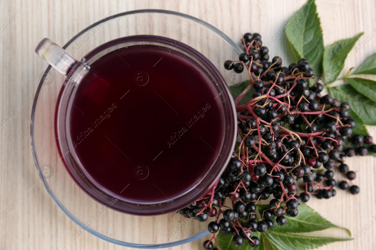 Photo of Glass cup of tasty elderberry tea with (Sambucus) berries on wooden table, closeup. Top view