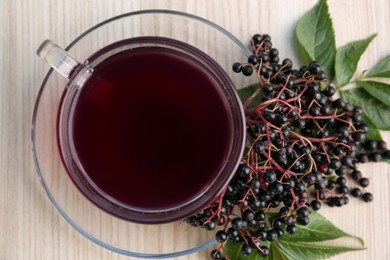 Glass cup of tasty elderberry tea with (Sambucus) berries on wooden table, closeup. Top view