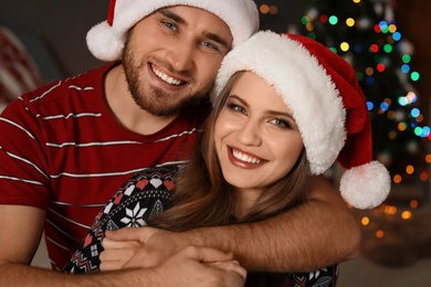 Photo of Happy young couple in Santa hats celebrating Christmas at home