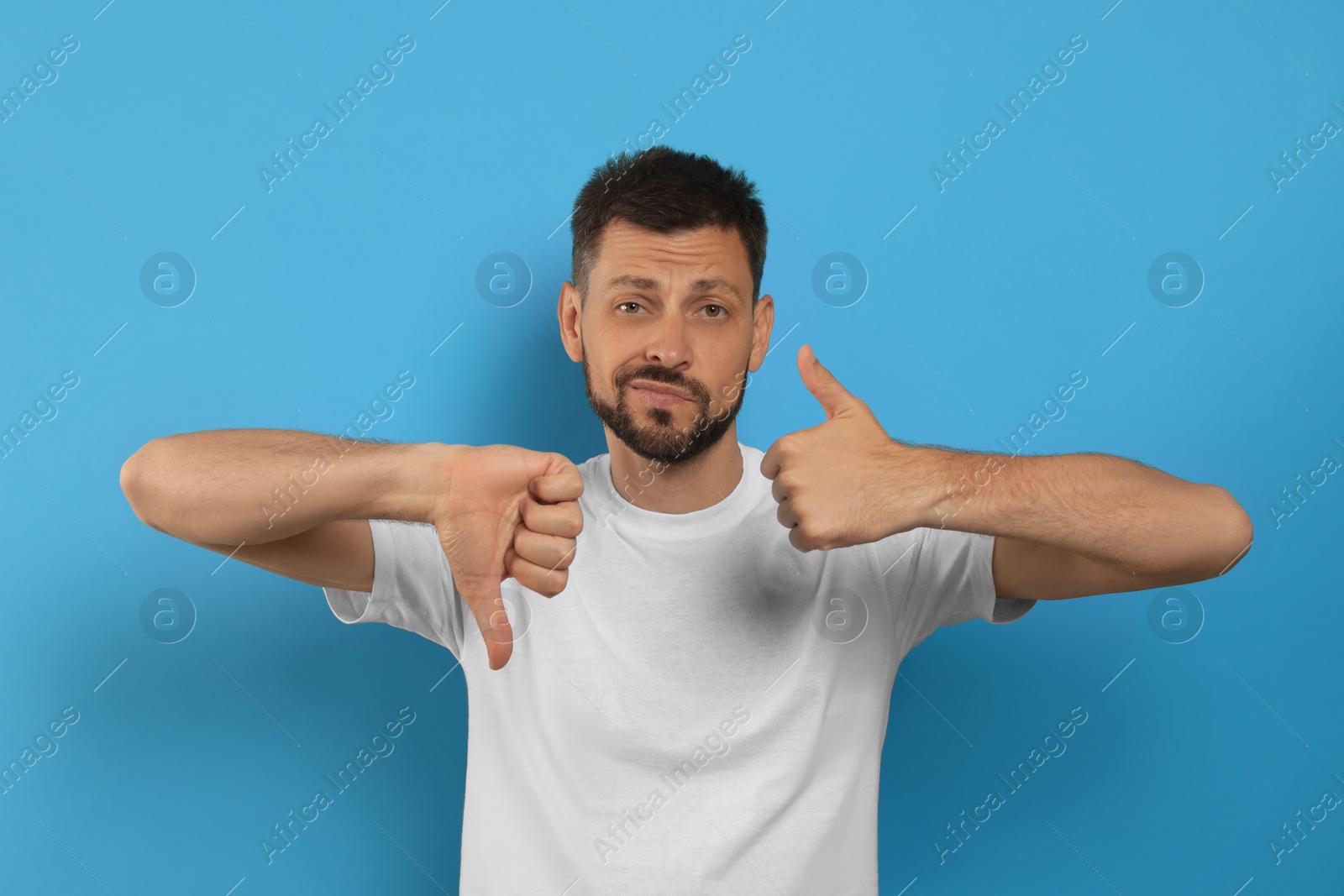 Photo of Man showing thumbs up and down on light blue background