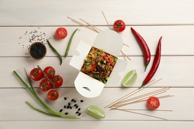 Photo of Box of wok noodles with vegetables and meat on white wooden table, flat lay