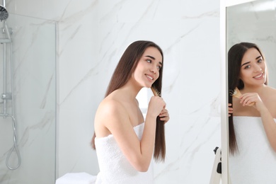 Photo of Beautiful young woman with hair brush looking into mirror in bathroom