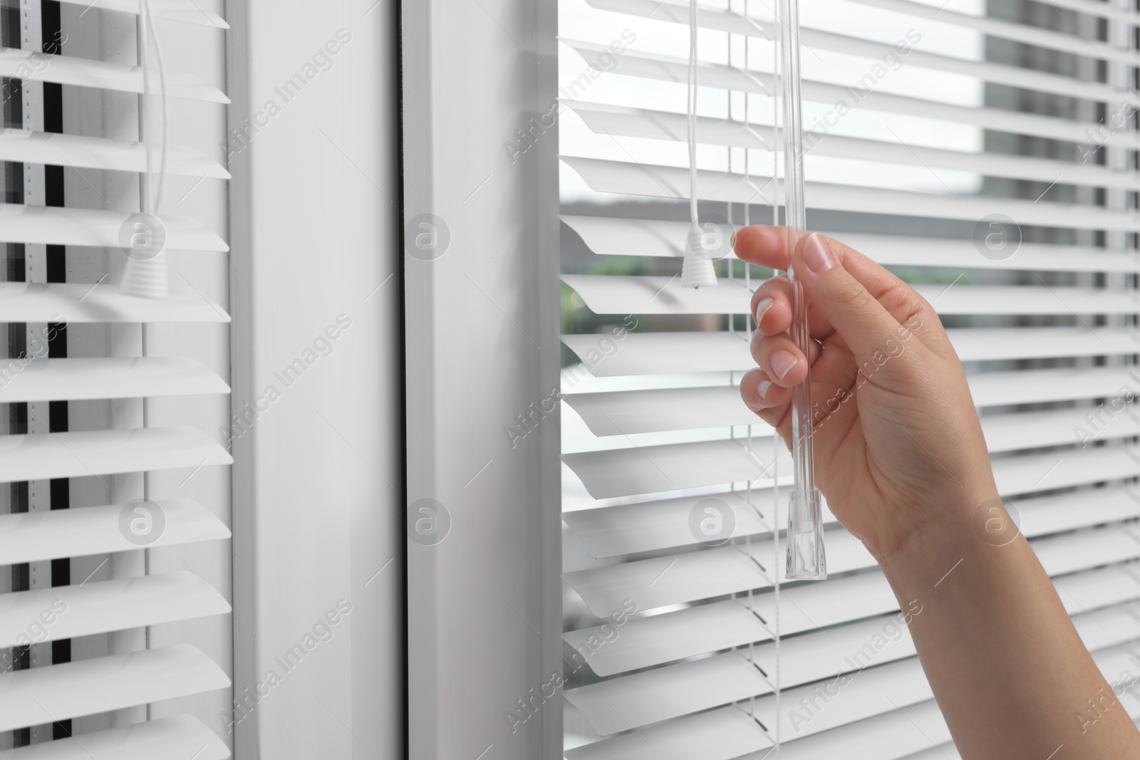 Photo of Woman opening horizontal blinds on window indoors, closeup. Space for text