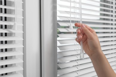 Photo of Woman opening horizontal blinds on window indoors, closeup. Space for text