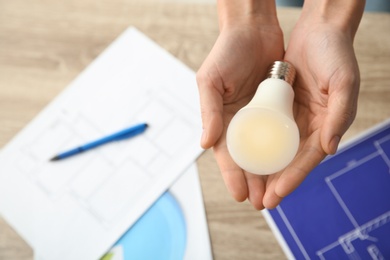 Photo of Woman holding lamp bulb over table with documents, closeup. Space for text