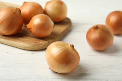 Photo of Ripe onions on white wooden table, closeup