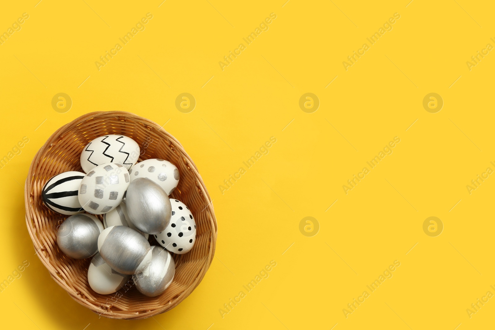 Photo of Wicker basket full of painted Easter eggs on color background, top view with space for text