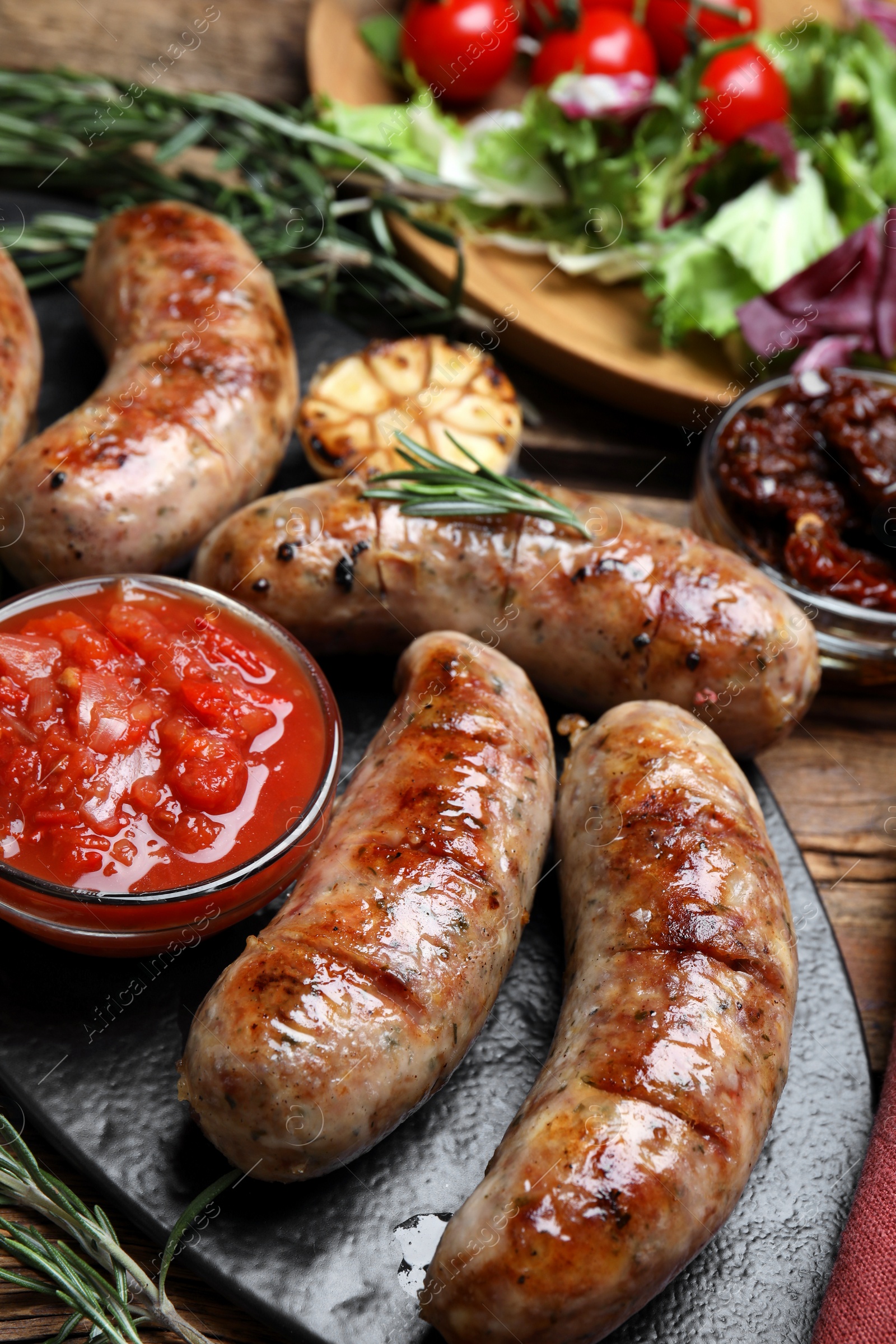 Photo of Tasty grilled sausages served with sauce on wooden table