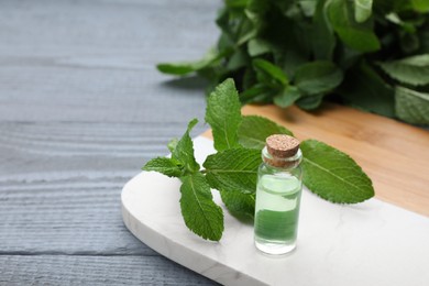Photo of Bottle of essential oil and mint on grey wooden table. Space for text