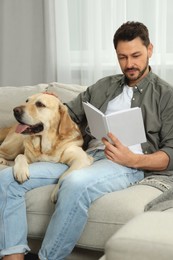 Man reading book on sofa near his cute Labrador Retriever at home