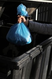 Photo of Woman throwing trash bag full of garbage in bin outdoors, closeup