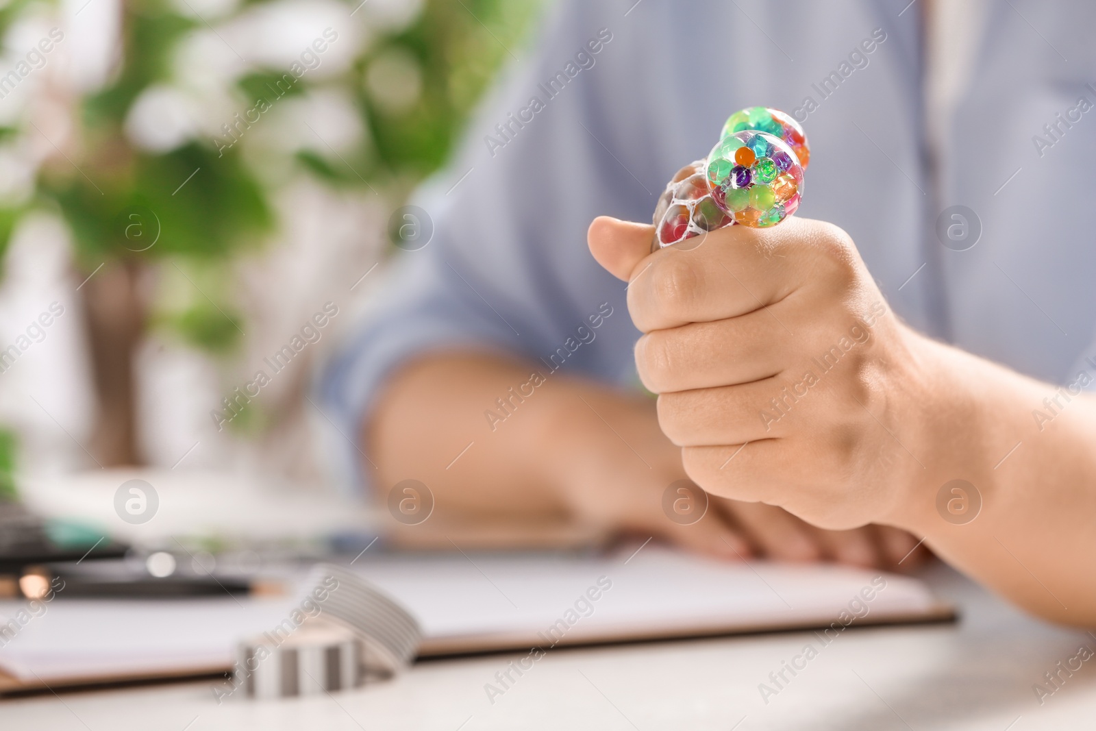 Photo of Woman squeezing colorful slime in office, closeup. Antistress toy