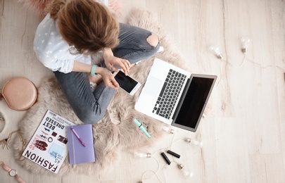 Female beauty blogger with smartphone and laptop indoors, top view