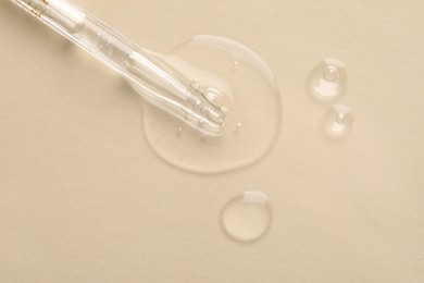 Glass pipette and transparent liquid on beige background, top view