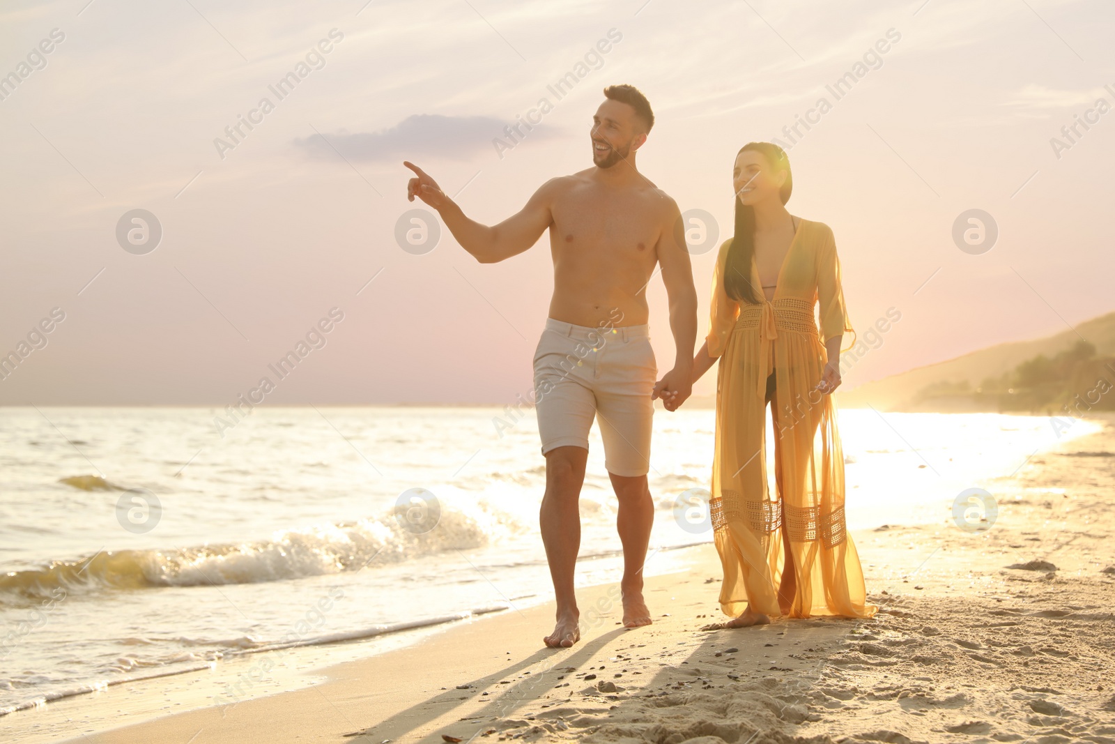 Photo of Happy young couple walking together on beach at sunset