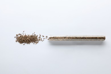 Photo of Glass tube with cumin seeds on white background, top view