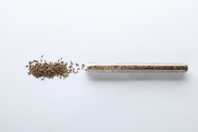 Glass tube with cumin seeds on white background, top view