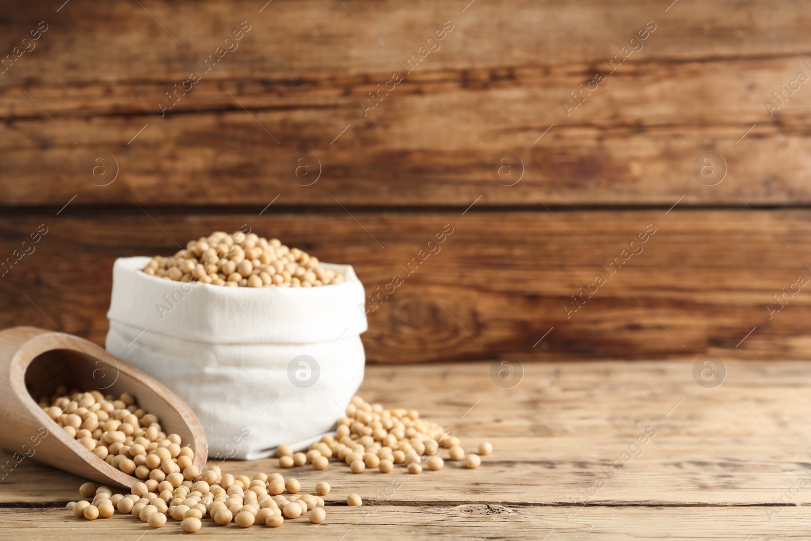 Photo of Scoop and sack with soy on wooden table, space for text