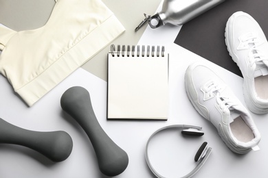 Flat lay composition with sportswear, notebook and dumbbells on color background. Gym workout plan