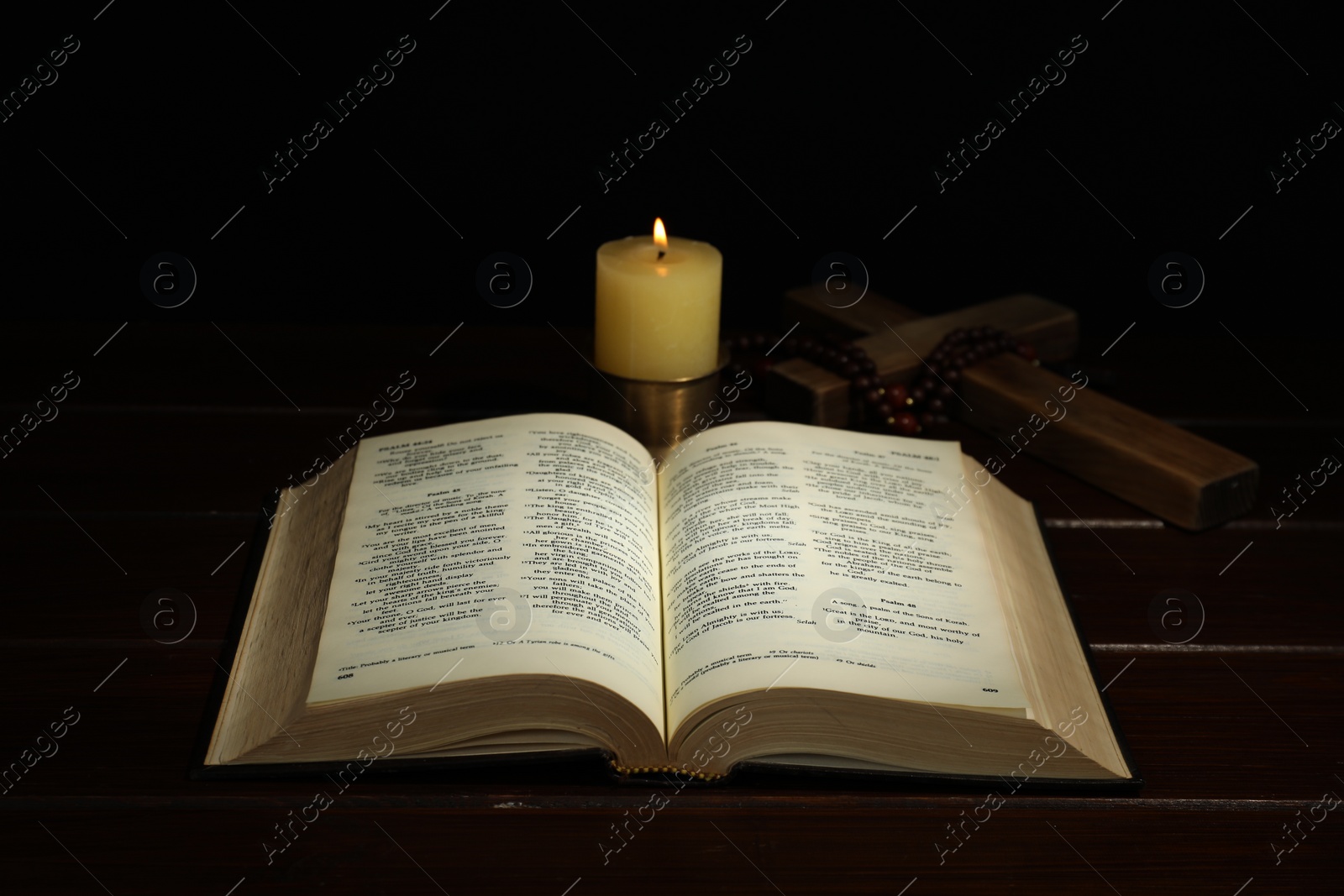 Photo of Church candle, Bible, cross and rosary beads on wooden table