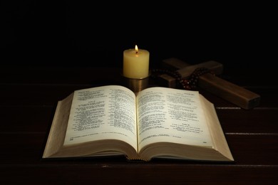 Photo of Church candle, Bible, cross and rosary beads on wooden table