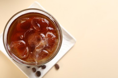 Photo of Refreshing iced coffee in glass on beige table, top view. Space for text
