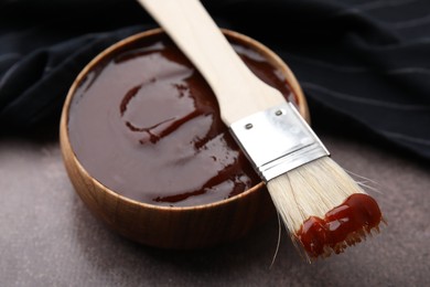 Photo of Marinade in bowl and basting brush on brown table, closeup