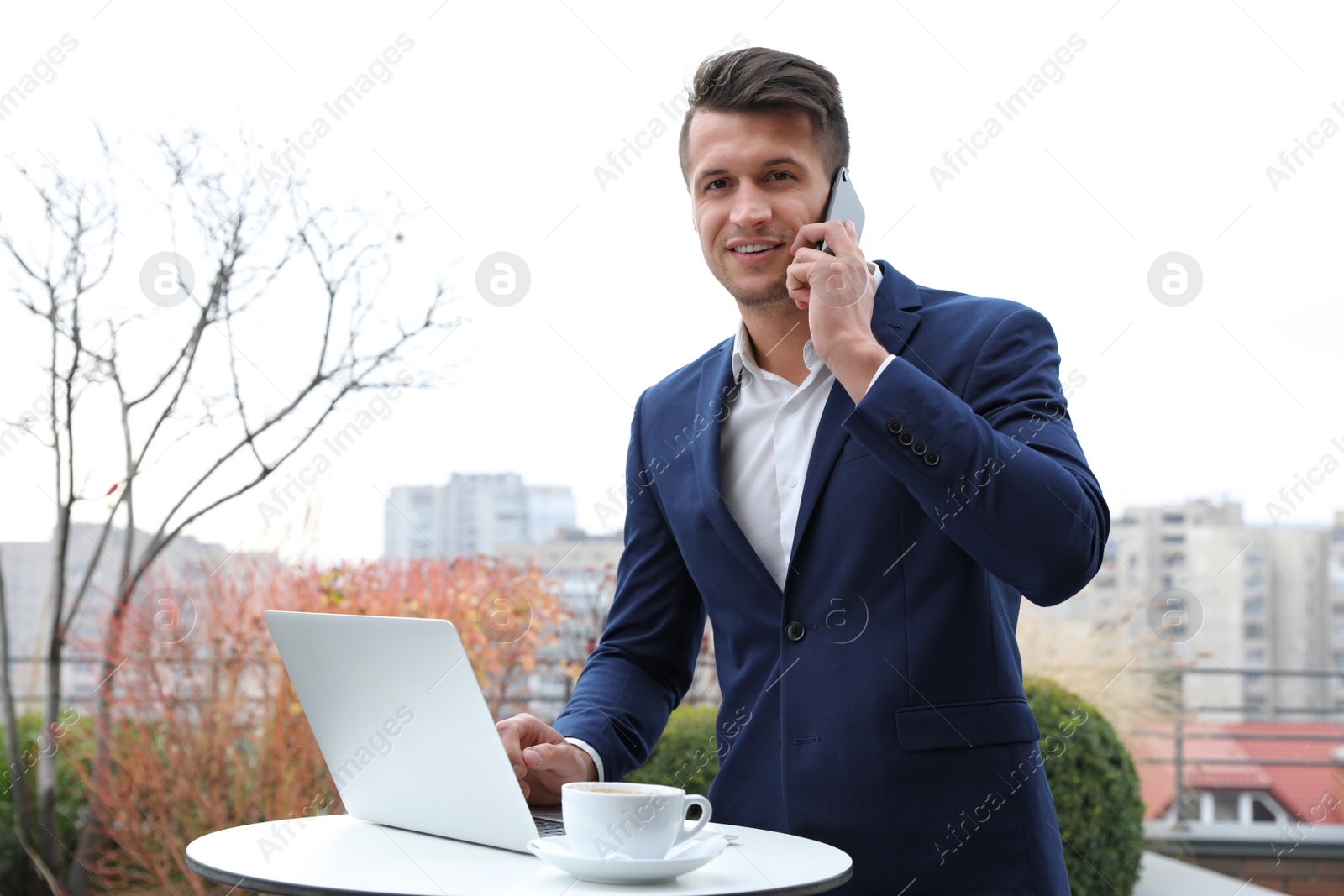 Photo of Businessman with laptop talking on phone in outdoor cafe. Corporate blog